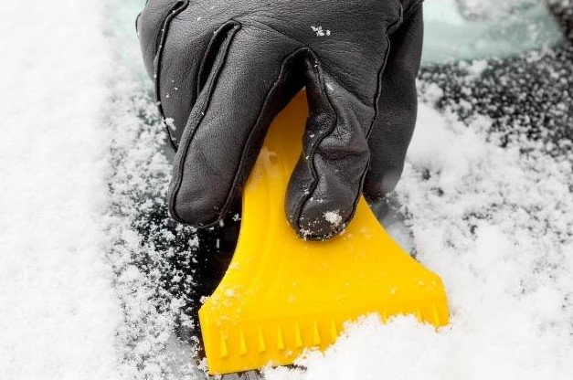 Gloved hand scraping ice with a yellow scraper